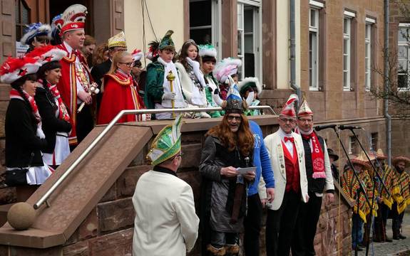 Prineznpaare, und Gardemädchen stehen auf einer Treppe vor dem Rathaus. Davor stehen auf einer kleinen Bühne der als Wikinger verkleidete Bürgermeister sowie vier Sitzungspräsidenten mit Narrenmütze. 