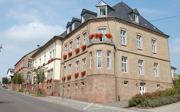 Großes Sandsteingebäude mit roten Blumen in den Fenstern.