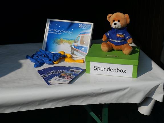 Grüne Spendenbox mit einem Teddybär und Flyern des Arbeiter-Samariter-Bundes