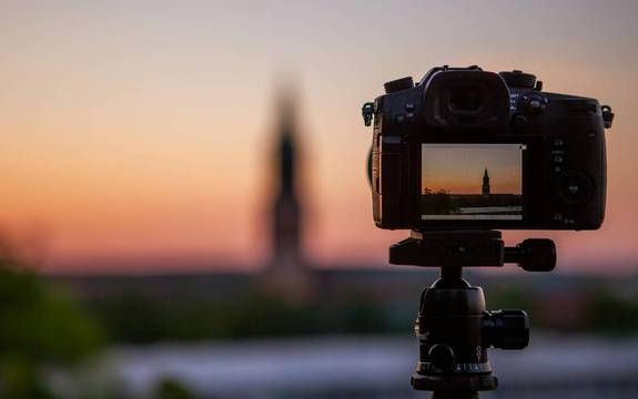 Fotokamera, die auf einem Stativ steht und den Sonnenuntergang hinter einem Turm fokussiert.