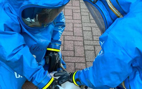 Zwei Feuerwehrleute in blauen Anzügen beugen sich über einen Plastikbehälter.