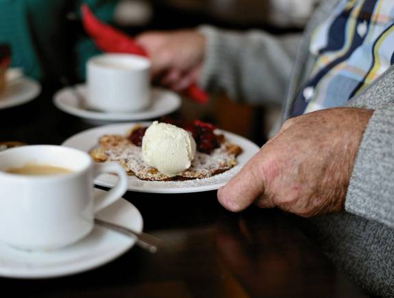 Detailaufnahme alter Mann mit Kaffetasse und Teller mit Waffeln und Eis