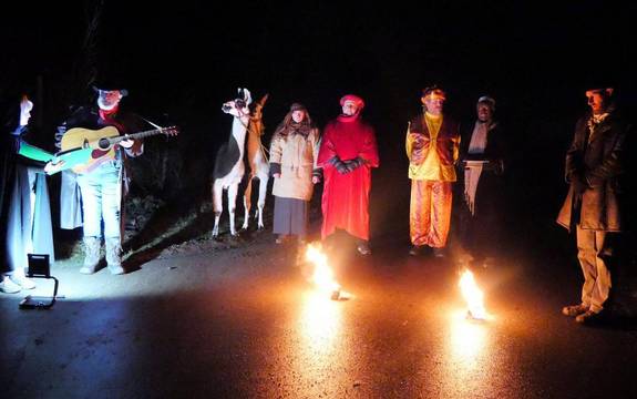 Schauspieler in bunten Gewändern stehen im dunkeln an einem Feuer.